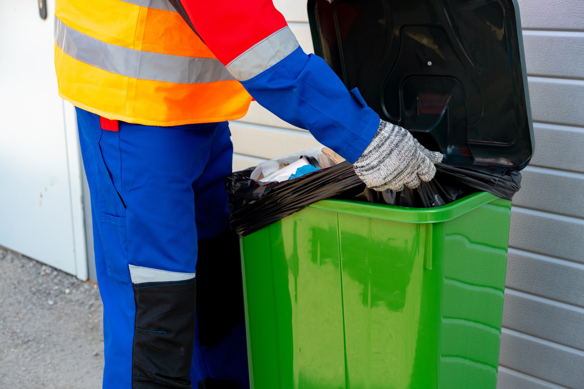 Janitor takes garbage out of trash container outdoors